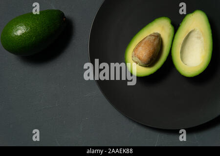 Fresche, crudo affettato avocado su una piastra nera su sfondo grigio Foto Stock