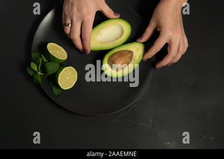 La donna la preparazione di materie di avocado e calce su una piastra nera su sfondi scuri Foto Stock