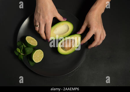 La donna la preparazione di materie di avocado e calce su una piastra nera su sfondi scuri Foto Stock