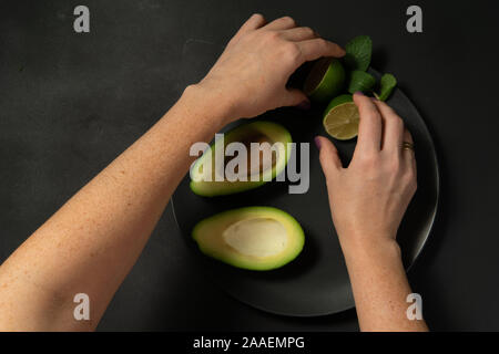 La donna la preparazione di materie di avocado e calce su una piastra nera su sfondi scuri Foto Stock