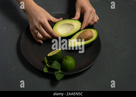 La donna la preparazione di materie di avocado e calce su una piastra nera su sfondi scuri Foto Stock