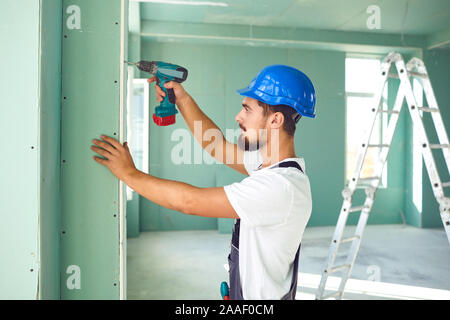 Lavoratore builder installa i pannelli in gesso cartonato muro a secco a una costruzione Foto Stock