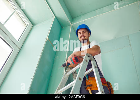 Un costruttore in piedi su una scala installa il muro a secco in corrispondenza di un sito in costruzione Foto Stock