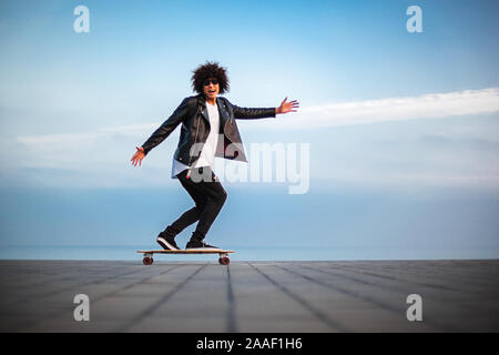 Bel giovane afro american ragazzo con lo skateboard con cielo blu, sfondo spazio copia Foto Stock