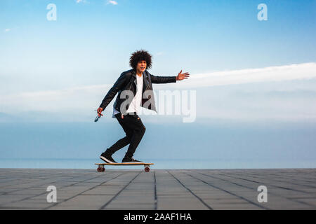 Bel giovane afro american ragazzo con lo skateboard con cielo blu, sfondo spazio copia Foto Stock