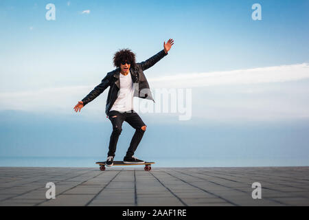 Bel giovane afro american ragazzo con lo skateboard con cielo blu, sfondo spazio copia Foto Stock