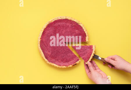 Bacche tradizionale concetto di torta con un rosso torta di mirtillo palustre su sfondo giallo. Donna di taglio e di prendere una fetta di torta. Christmas Festive dessert. Foto Stock