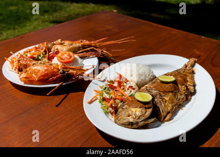 Piastre con gamberoni e fritture di pesce oceano con il lato piatto e insalata su di un tavolo di legno. Foto Stock