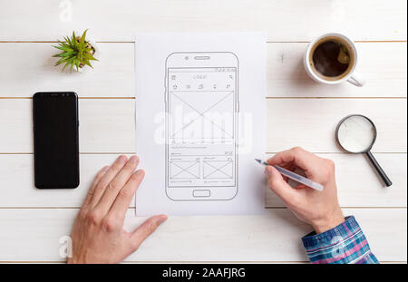 Il web designer bozzetti l'interfaccia utente del wireframe del telefono mobile. Scrivania, vista dall'alto, piatto comosition laici. Foto Stock