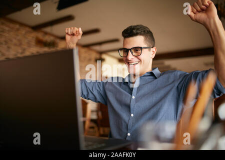 Bel uomo d affari con computer portatile avente le braccia con i pugni sollevato, celebrando il successo. Felice freelancer hipster in bicchieri terminato il lavoro sul progetto Foto Stock