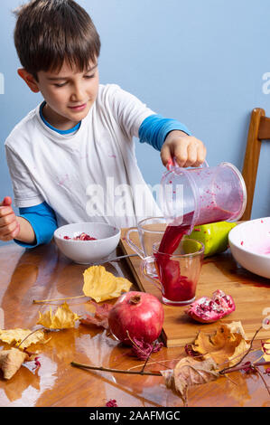 Ragazzo giovane spremitura e versare il succo di melograno, facendo un pasticcio. Viso e vestiti sporchi con macchie rosse. In autunno un sano concetto. Foto Stock