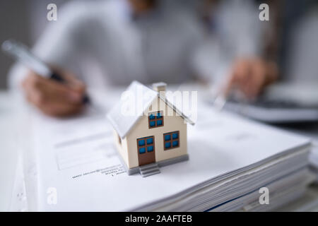 Imprenditore il canto il calcolo di una fattura con il modello della casa in ufficio Foto Stock