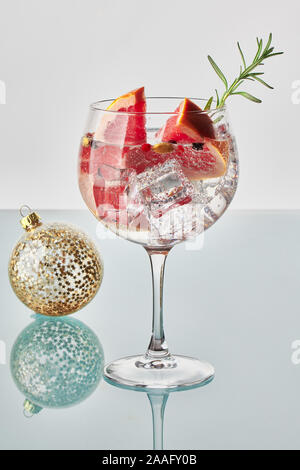 Un bicchiere di gin tonic con fette di pompelmo, verde rosmarino, cubetti di ghiaccio e la palla di Natale Foto Stock