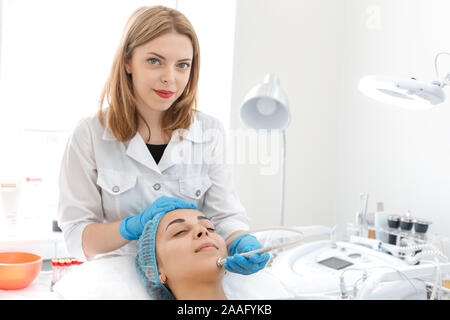 Estetista fa un giovane bella ragazza un trattamento del viso trattamento sotto vuoto la procedura. Cura del viso e il ringiovanimento. Aumento del tono epidermico. Foto Stock