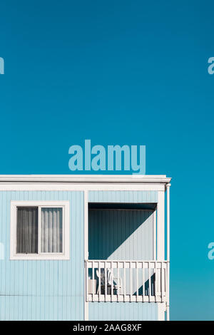 Vista artistico di lonely basic blue hotel/condominio deck e sedia in plastica contro il cielo blu Foto Stock