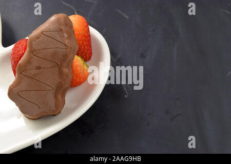 Il cioccolato albero di Natale e fragole fresche sul cuore piastra sagomata sulla cima di una lavagna sfondo. Abbondanza di spazio copia. Foto Stock