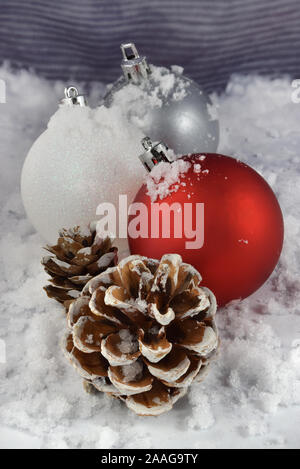 Rosso, bianco e argento Natale ornamenti e Snow capped Pigne in un bianco scena invernale Foto Stock