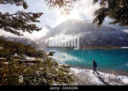 Turistico con zaino e fotocamera passeggiando lungo la spiaggia di neve al lago di montagna in Kazakistan e in Asia centrale Foto Stock