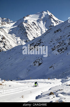 Ciclista corse in strada di neve sulle montagne di Almaty, Kazakhstan Foto Stock