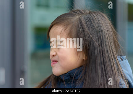 Giovane ragazza asiatica in giacca nera con disgusto grimace sul suo viso outdoor close-up ritratto laterale con spazio di copia Foto Stock