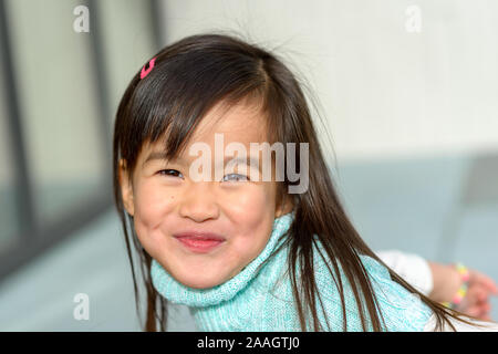 Incantevole piccola ragazza asiatica con un malizioso sorriso giocoso grinning presso la telecamera in un bel blu collo polo top Foto Stock