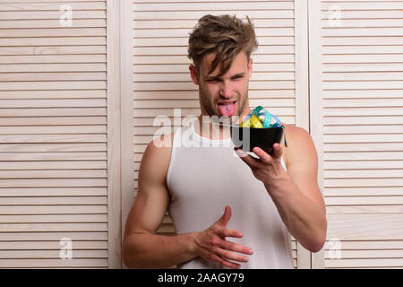 Uomo con faccia disgustata espressione guarda la ciotola con nastro di misurazione all'interno sullo sfondo della persiana di colore beige Foto Stock