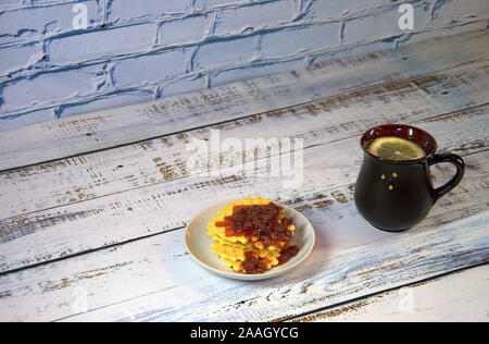Una ceramica nera tazza da tè con limone e piattino con una pila di cialde Viennese con confettura di fragole. Close-up. Foto Stock
