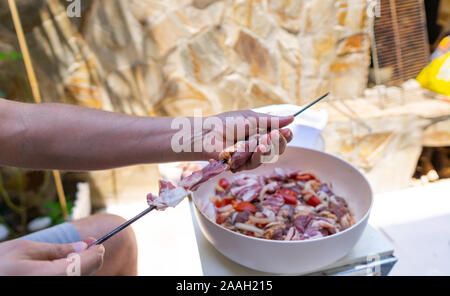 Le mani di un uomo di mettere carne su spiedini per barbecue. Close-up immagine della carne cruda su spiedino. Foto Stock