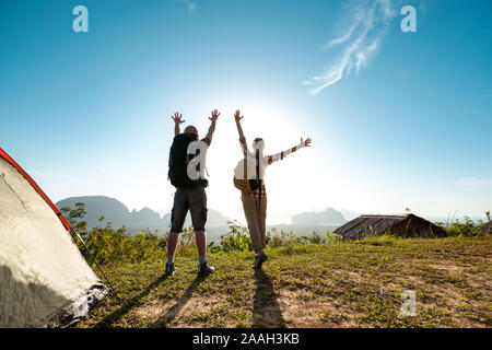Due felici gli escursionisti maschio e femmina sta con le braccia sollevate a sunrise vicino alla tenda Foto Stock