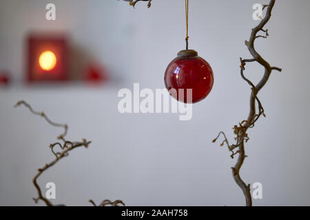 Close up di un rosso palla di Natale presso una filiale di fronte un unsharp sfondo in bianco e rosso Foto Stock