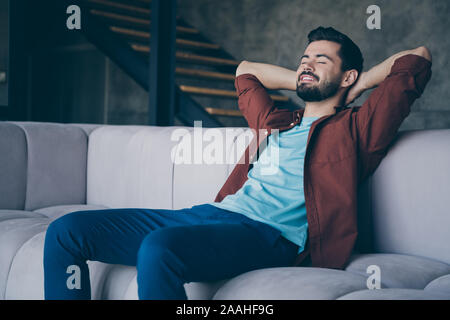 Foto del bel ragazzo in alta spiriti tenendo le mani dietro la testa seduta confortevole lettino grande sonno rilassante sabato mattina in appartamento moderno Foto Stock