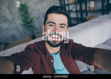 Foto del bel ragazzo nel soggiorno godetevi weekend rendendo selfies parlando di skype con amici che mostra appartamento nuovo e moderno appartamento in interni vestiti casual Foto Stock