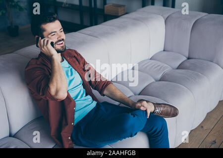 Foto del profilo del bel ragazzo tenendo il telefono vicino a orecchio ascoltando amici stranieri chatterbox accogliente Sit divano nel soggiorno moderno appartamento in ambienti interni Foto Stock