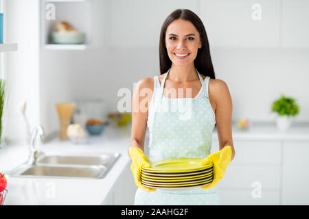 Pulire le piastre concetto, bella fatta trattenere pile di piatti ha lavato con giallo guanti protettivi in gomma si sentono contenuto nella dispersione di luce cucina bianco Foto Stock