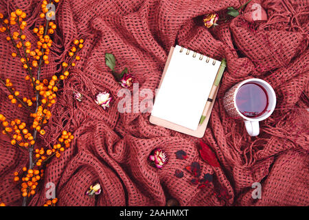 Composizione d'autunno. Tazza di tae, coperta, notebook con penna, rosa appassita. Appartamento laico, vista dall'alto, spazio di copia Foto Stock