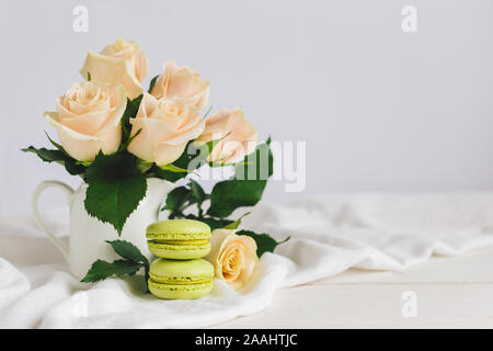 Due verde chiaro macarons francese con tenera Rose in un vaso su sfondo bianco. Close up. Il pistacchio macarons. Posto per il testo. Foto Stock