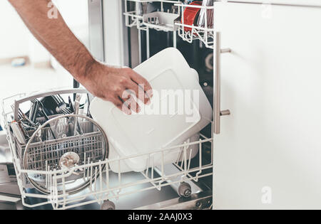 Close-up di persona lo svuotamento o il caricamento di lavastoviglie in cucina Foto Stock