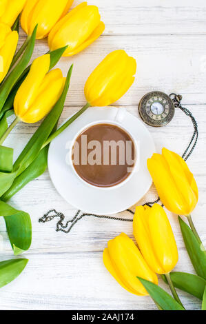 Tulipani gialli, una tazza di caffè, cappuccino e vintage guarda su una catena su un bianco sullo sfondo di legno Foto Stock