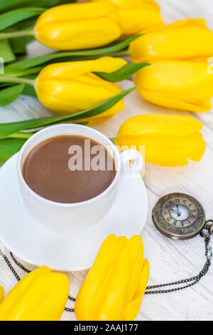 Tulipani gialli, una tazza di caffè, cappuccino e vintage guarda su una catena su un bianco sullo sfondo di legno Foto Stock