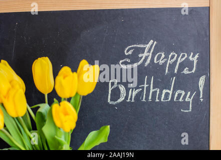 Un mazzo di tulipani gialli e la scritta in gesso "Happy Birthday" su una lavagna Foto Stock
