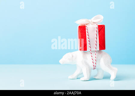 Un giocattolo bianco recano offrendo in rosso di un regalo di Natale su sfondo blu. Conceptual Anno Nuovo card. Foto Stock