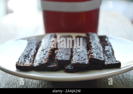 Croccante di cioccolato fondente stick mangiare pane giovane con caffè in tazza rossa Foto Stock
