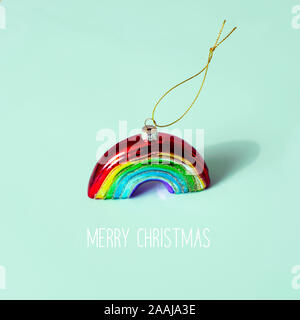 Un ornamento di Natale a forma di arcobaleno e il testo buon natale su uno sfondo verde Foto Stock