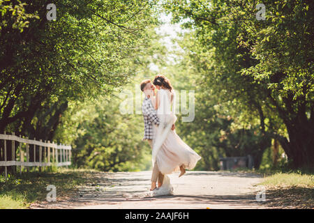 Felice sposo solleva sposa in estate park. uomo sollevato e abbraccio donna per le sue braccia. Appena sposata giovane nel parco. Appena sposato. Passeggiata nel parco Foto Stock