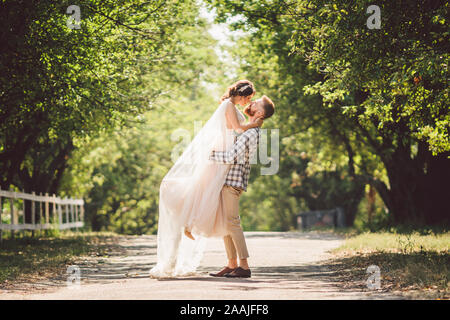 Felice sposo solleva sposa in estate park. uomo sollevato e abbraccio donna per le sue braccia. Appena sposata giovane nel parco. Appena sposato. Passeggiata nel parco Foto Stock