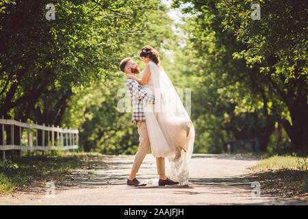 Felice sposo solleva sposa in estate park. uomo sollevato e abbraccio donna per le sue braccia. Appena sposata giovane nel parco. Appena sposato. Passeggiata nel parco Foto Stock
