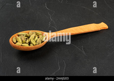 Verde cardamomo in cucchiaio di legno su sfondo scuro Foto Stock