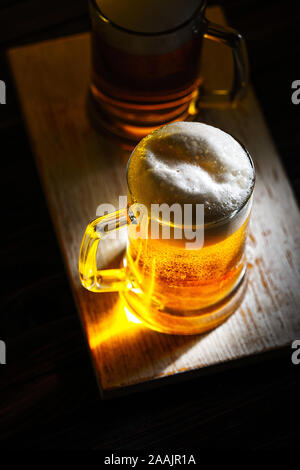 Due leggeri boccali da birra con schiuma bianca sul legno scuro tavolo. Vista da sopra Foto Stock