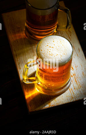 Due leggeri boccali da birra con schiuma bianca sul legno scuro tavolo. Vista da sopra Foto Stock