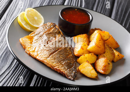 Piatto principale fried dorada filetto con patate guarnite e salse close-up su una piastra sul tavolo orizzontale. Foto Stock